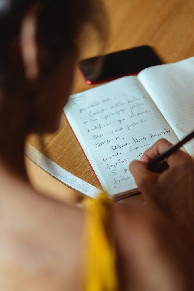 A focused scene of someone writing in a notebook, accompanied by a smartphone placed on the table.