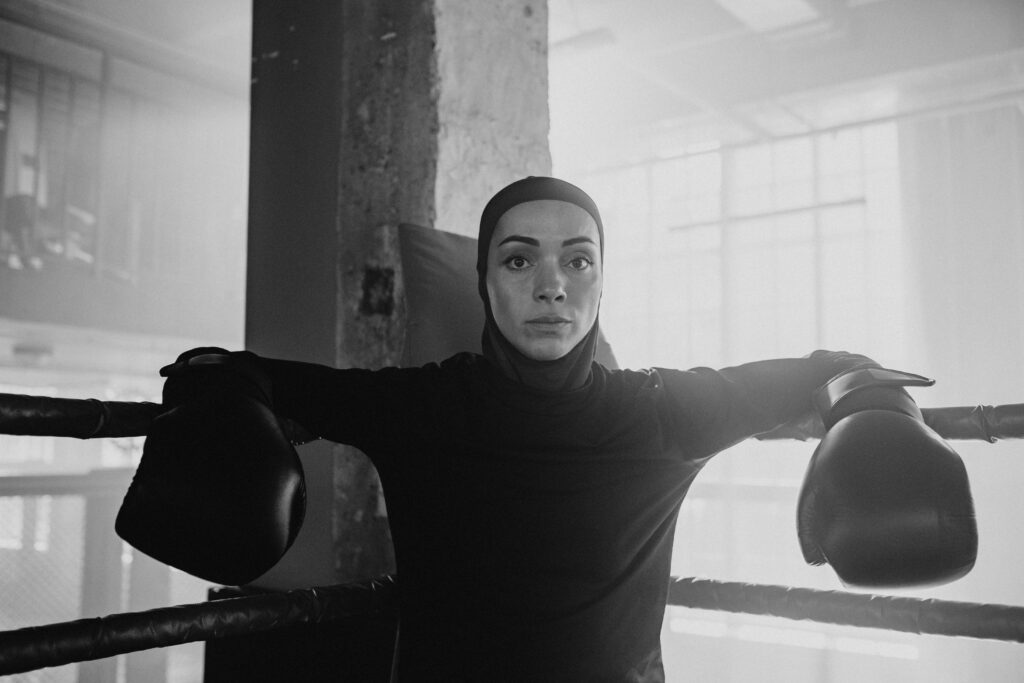 A focused female boxer in a hijab standing in a boxing ring, ready for training.